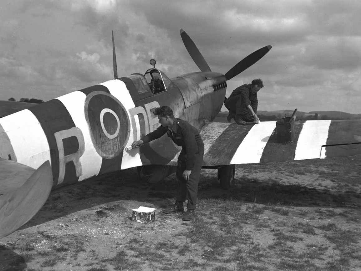 Men painting white stripes on an airplane's wings, 1944.