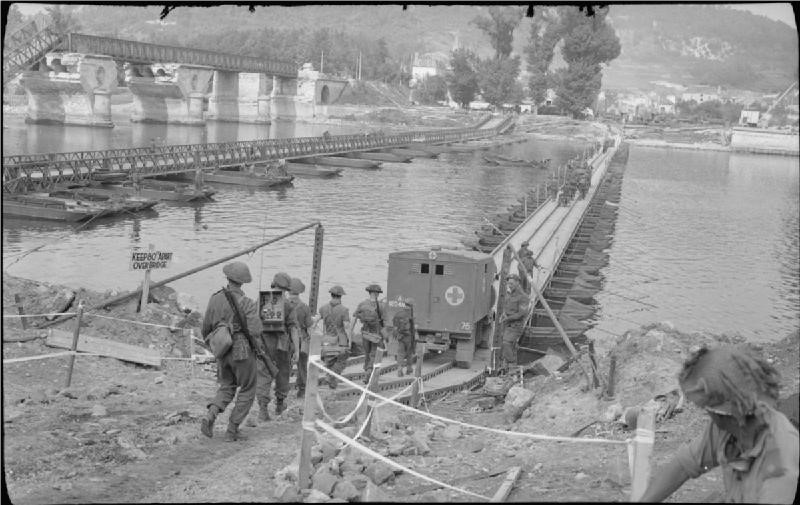 Men and trucks crossing a river on an improvised bridge. 