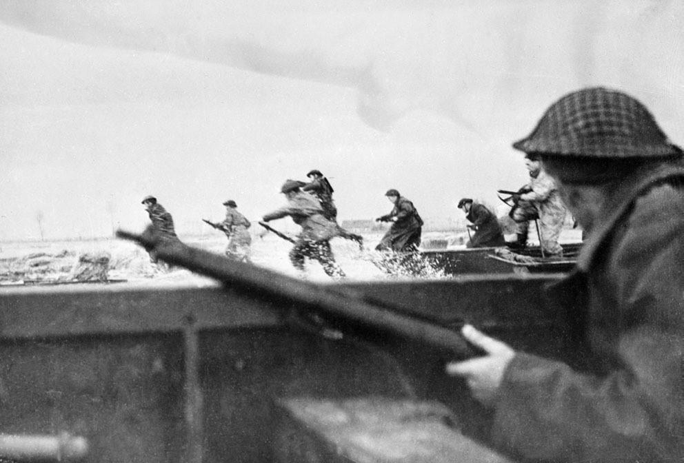 Photo of a man holding a rifle on a boat, with men in the background jumping into the water.
