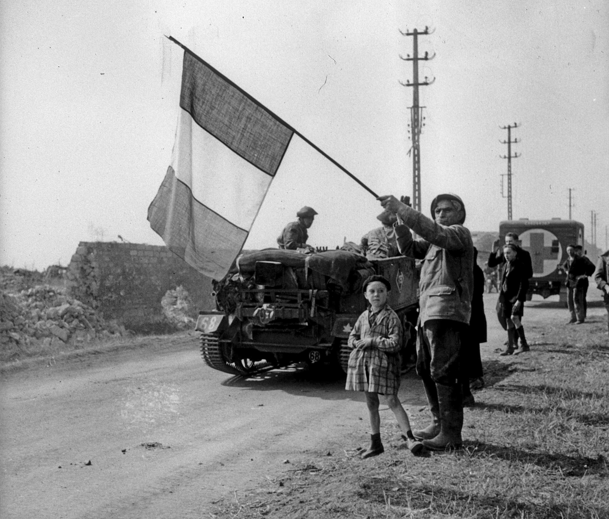 A man waves a French flag as military vehicles drive past.