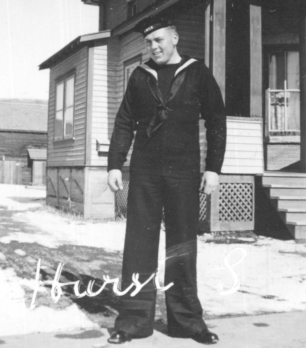 Black and white photo of a man in naval uniform standing outside a house.