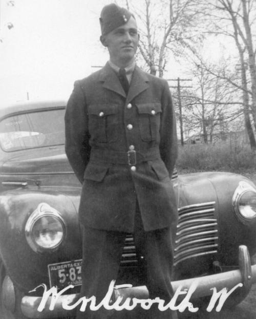 Black and white photo of a man standing with his hands behind is back, wearing a World War Two Air Force uniform.