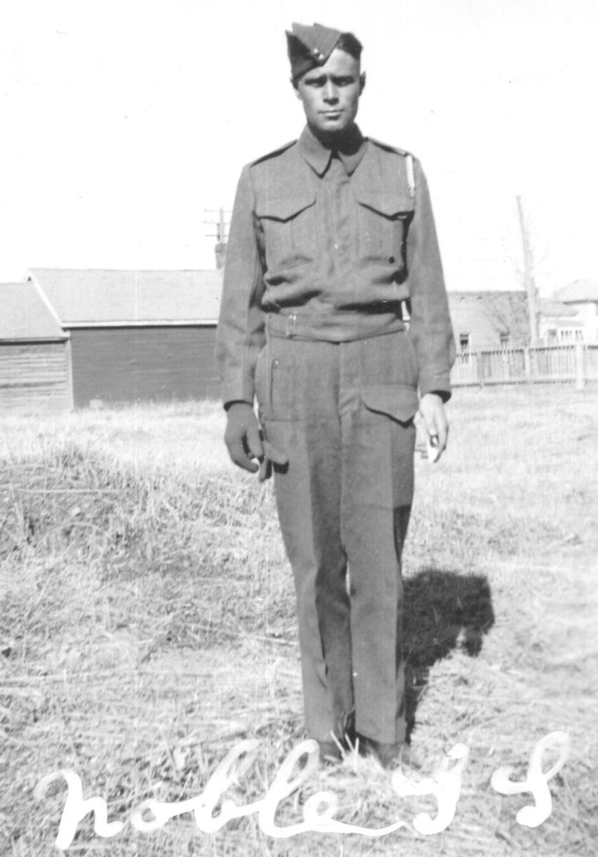Black and white photo of a man in World War Two uniform standing in a field.
