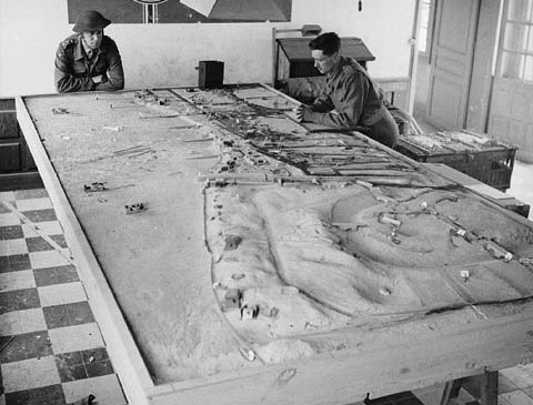 Two soldiers look at a 3D model of the beaches at Normandy.