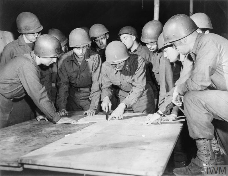 A group of men in military uniforms gather round a map on a table.