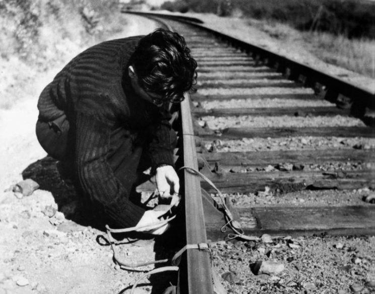 A man kneels next to a railroad track.