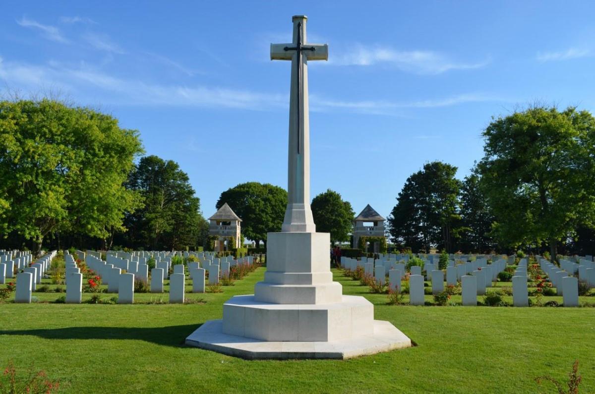 A white monument with a cross in front of many rows of white gravestones.