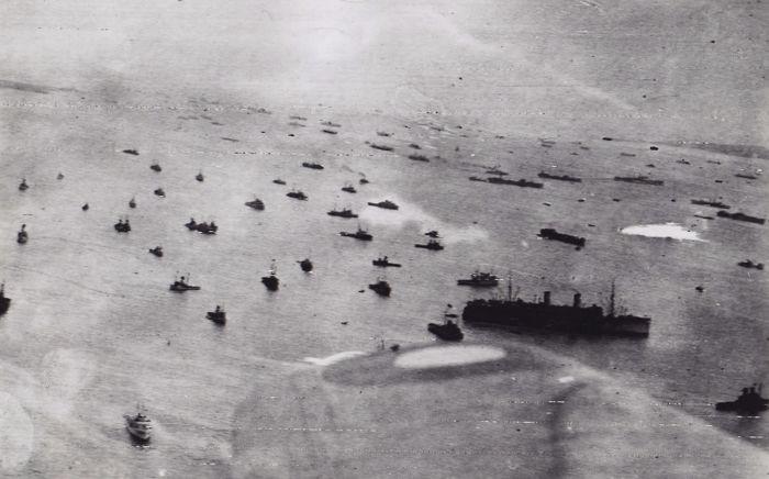 Aerial photo of dozens of ships in the water near Normandy.