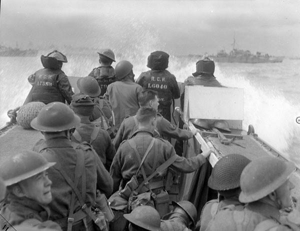 Photo of about 12 men in a landing craft heading for the shore at the coast of Normandy.