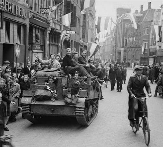 Dutch civilians sitting on a tank waving flags. Black and white photo from 1945.