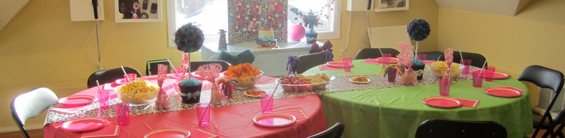 Two round tables with pink and green tablecloths set up for a birthday part with paper plates and pink and green decorations.
