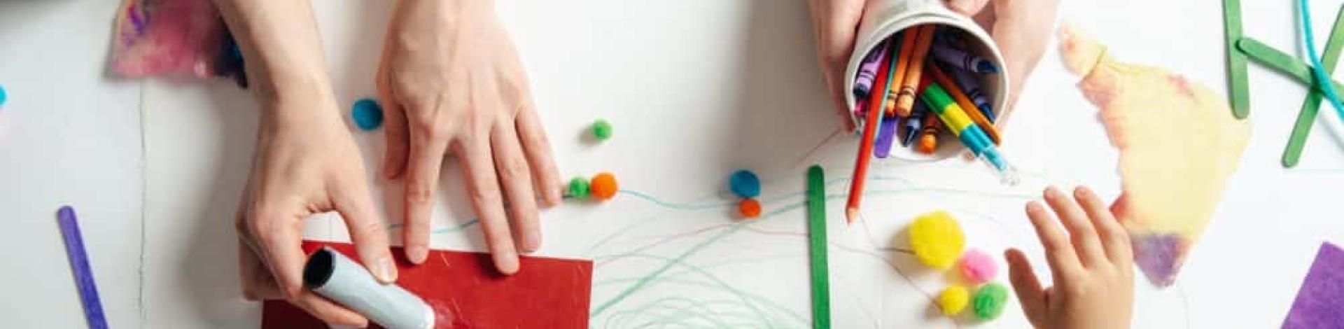 Hands of children photographed from above while they are colouring with markers and paint. 