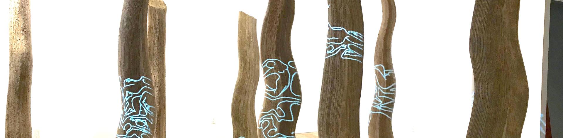 Tree trunks made of cardboard stand in an empty room, with swirling blue projections shining on them.
