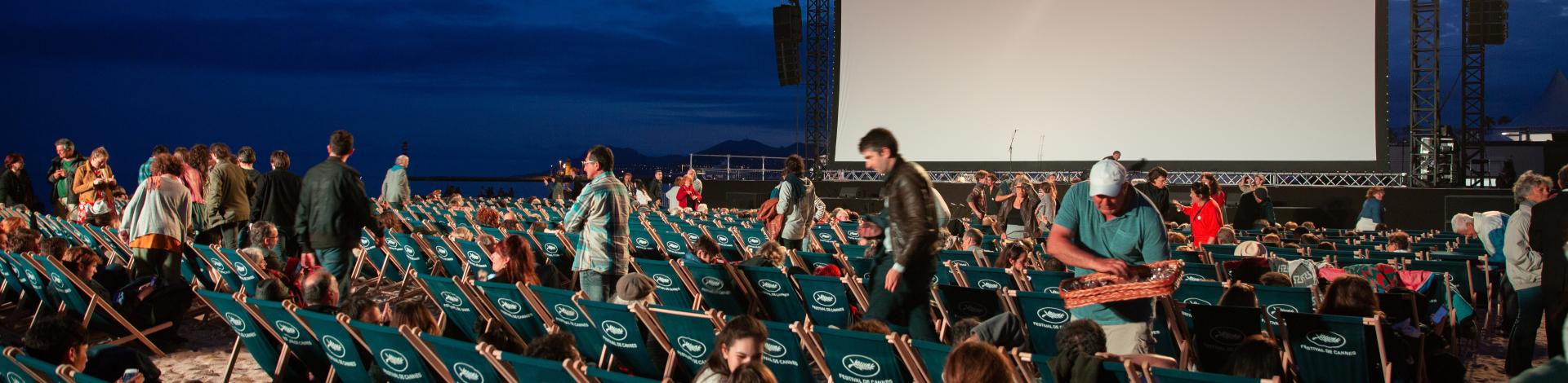 Outdoor movie screen with dark background and rows of people looking at the screen