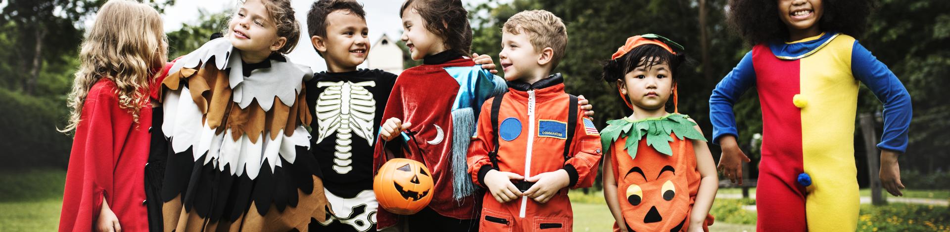 seven children dressed up in various Halloween costumes in a grass field 
