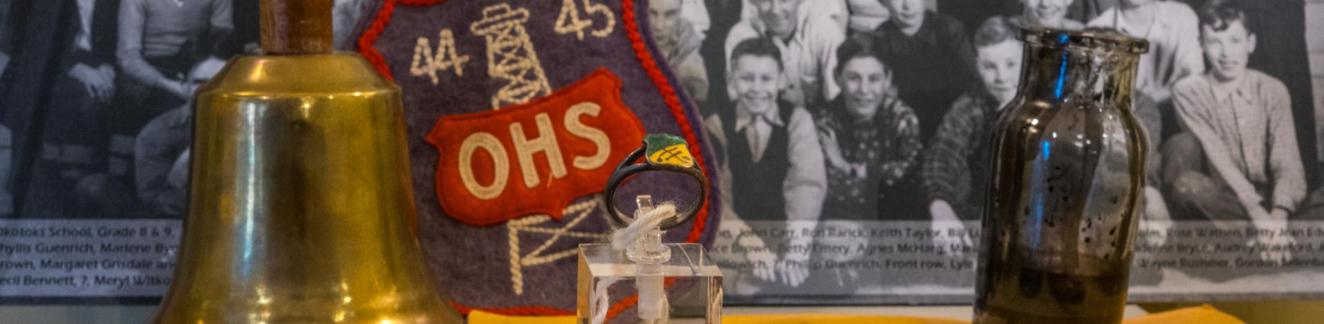a photo of old school items including a class ring, old class photo and a hand bell
