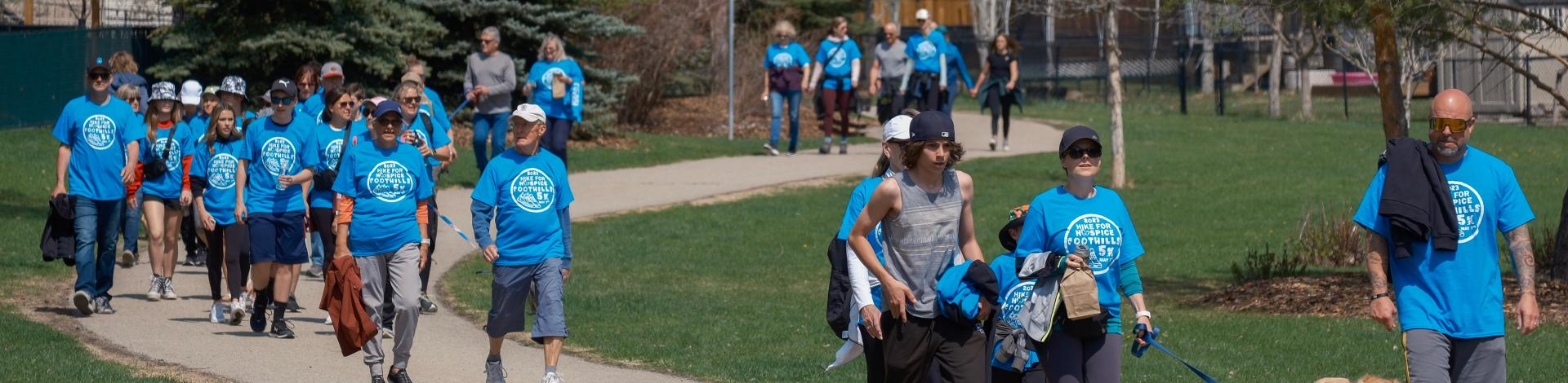 people in blue shirts walk pathways. The shirts say "hike for hospice"