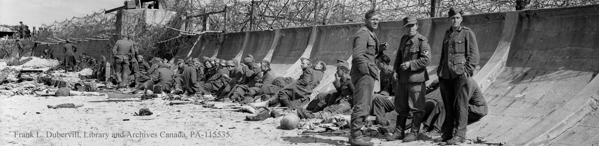 Black and white photograph of wounded men lying on the beach at Normandy.