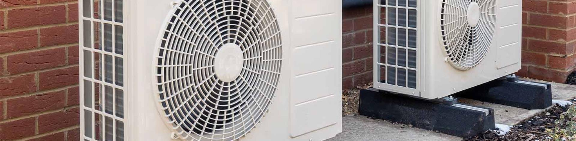 Two heat pumps angled along a red brick wall