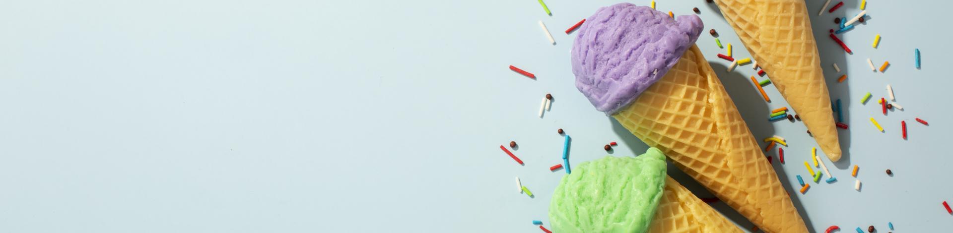 colourful ice cream cones surrounded by sprinkles with a light blue background