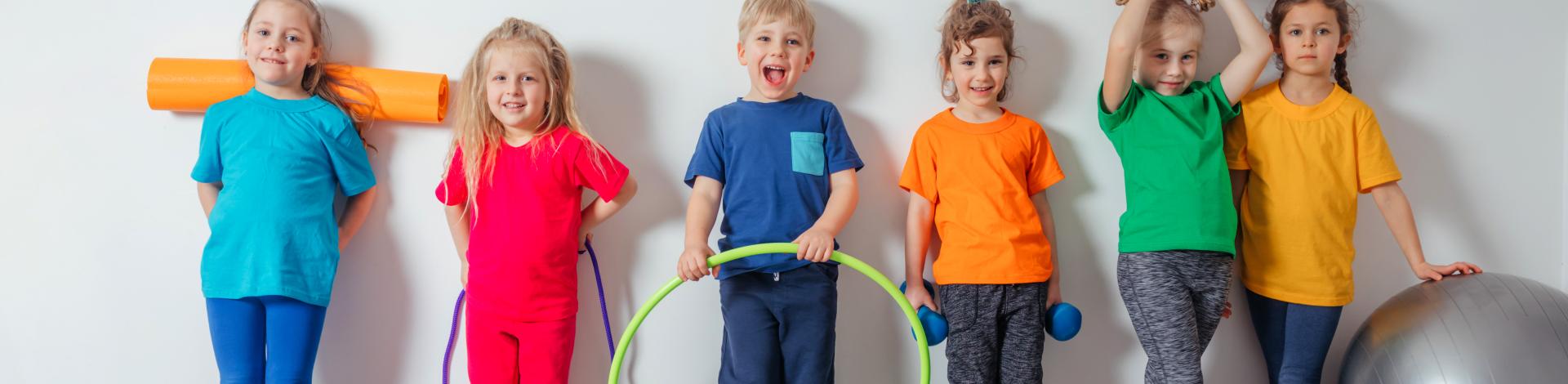 six smiling children lined up against a wall with fitness equipment