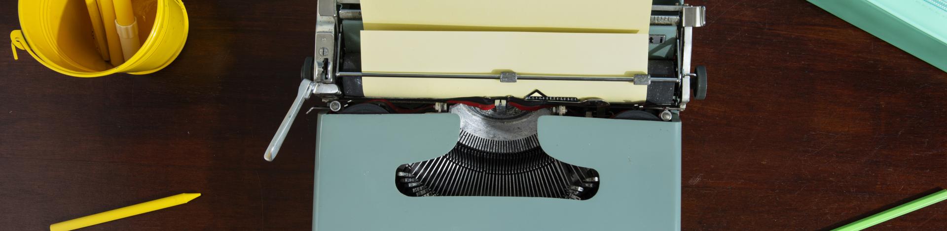 grey typewriter with yellow pencils and a green apple on a desk