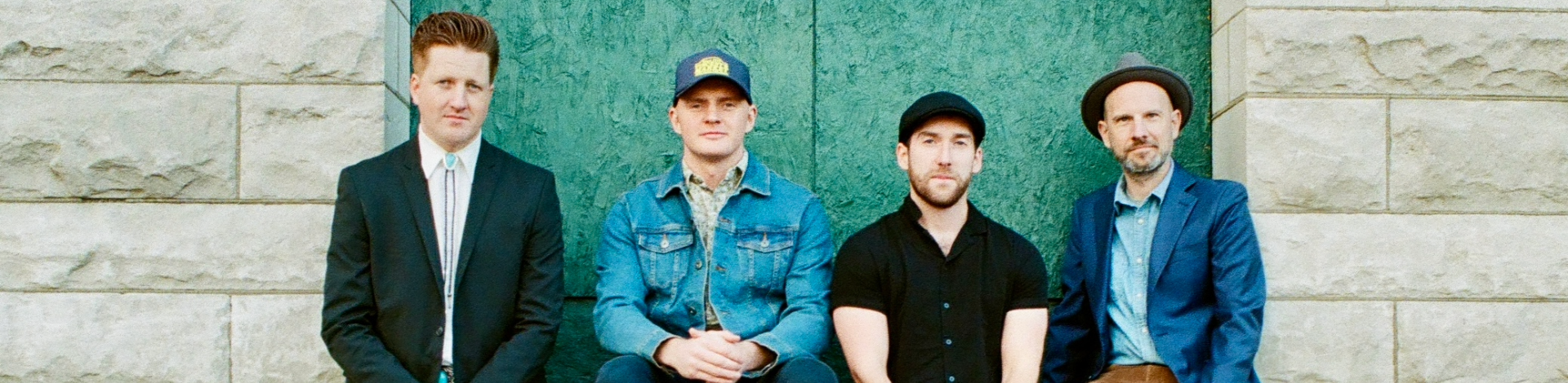 four members of the band jigjam pose on a wall