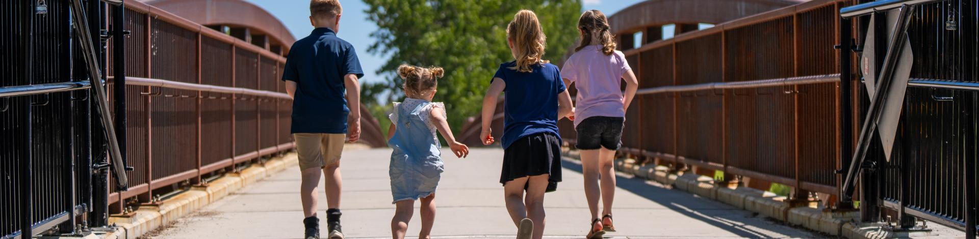 4 children holding hands walking on bridge