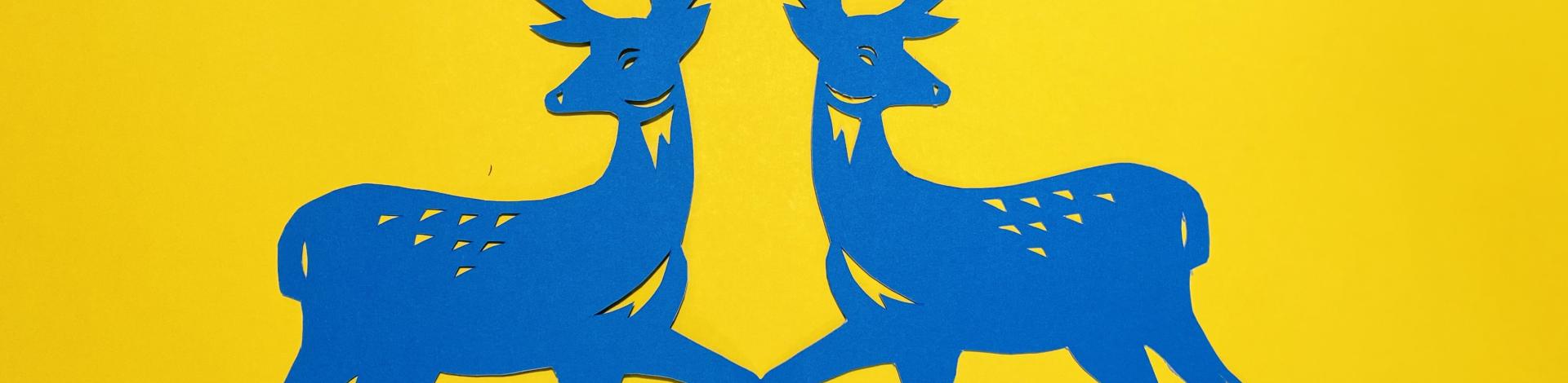Two blue stags made of paper on a yellow background.