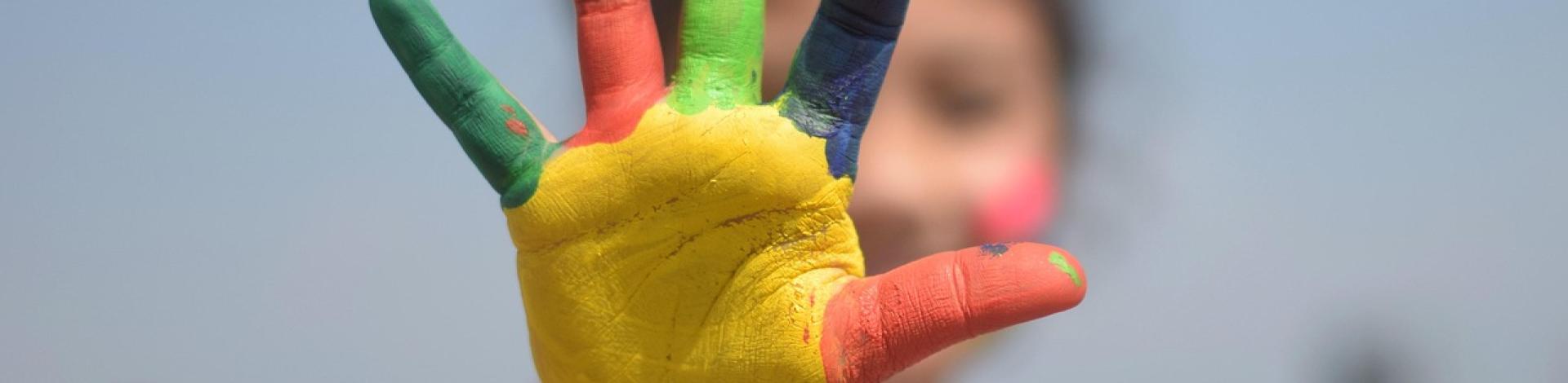 A child holds a hand toward the camera, the palm and each finger is covered in paint.