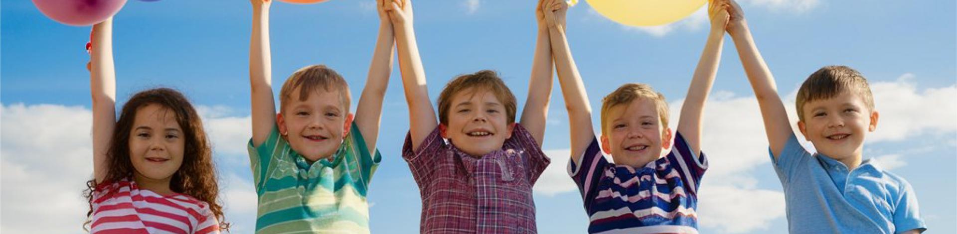 Five children in a field holding balloons above their heads.