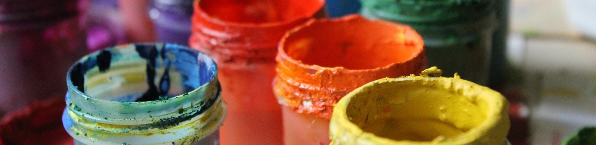 Open pots of paint sitting on a table, yellow, orange, red, green and blue.