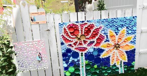 A flower made out of bottle caps on a white fence.