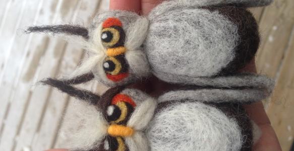 Two felted owls lying in a person's hand.