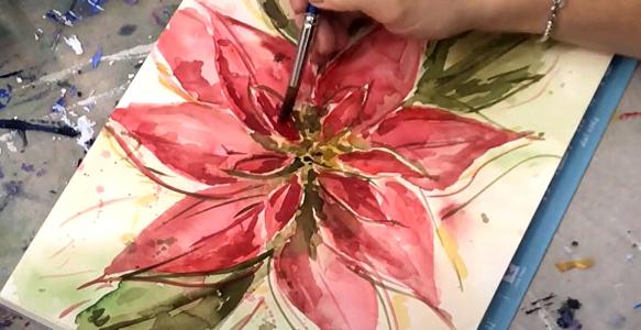 A hand holds a paintbrush over a watercolour painting of a red poinsettia flower. 