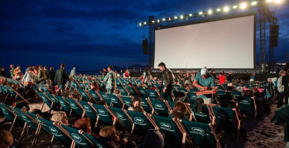 Outdoor movie screen with dark background and rows of people looking at the screen