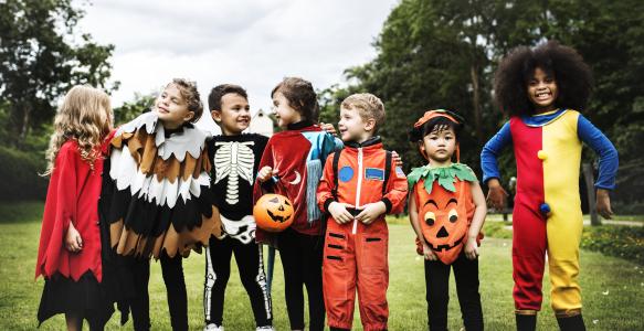 seven children dressed up in various Halloween costumes in a grass field 
