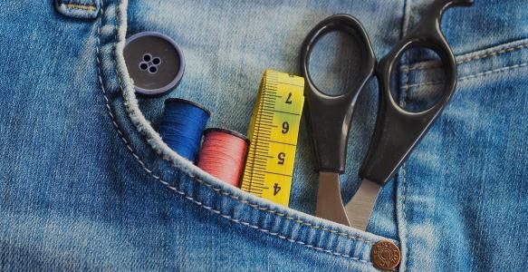 Scissors, tape measure, and thread in the pocket of a pair of jeans.