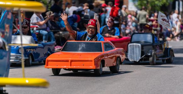 a tiny car in the okotoks parade. The man driving it is waving 