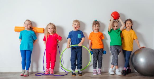 six smiling children lined up against a wall with fitness equipment
