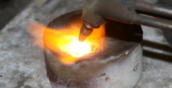 An acetylene torch is melting metal in a stone mould.