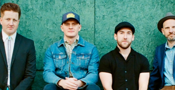 four members of the band jigjam pose on a wall