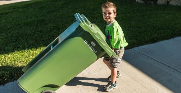 Boy putting out green organics cart at curb for collection