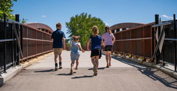 4 children holding hands walking on bridge