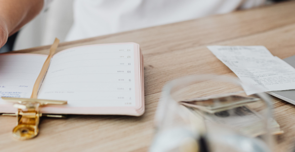 an open notebook with a computer and receipts and money stacked beside
