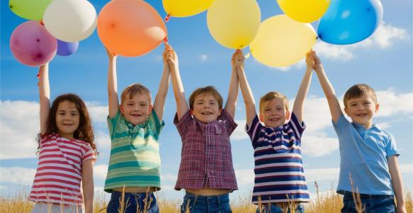 Five children in a field holding balloons above their heads.