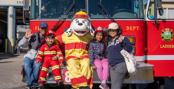 A family of four poses with Sparky in front of a Firetruck