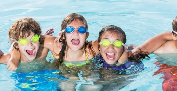 five children smiling in a pool wearing goggles