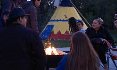 People gathered around a firepit in front of Okotoks Tipi for Fireside Stories