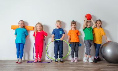 six smiling children lined up against a wall with fitness equipment